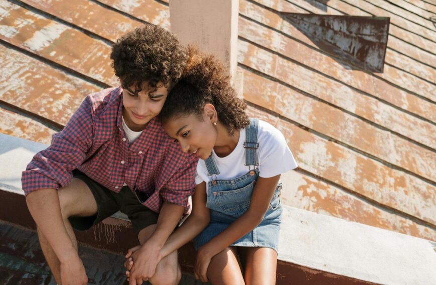 Teen couple sitting close on a sunny rooftop, sharing a tender moment.