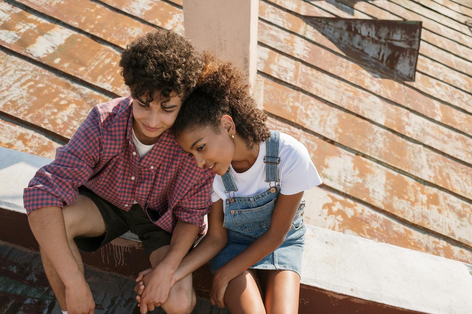 Teen couple sitting close on a sunny rooftop, sharing a tender moment.
