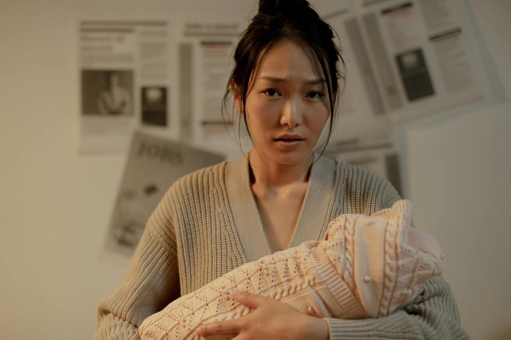A concerned mother embraces her newborn indoors, surrounded by newspaper articles.