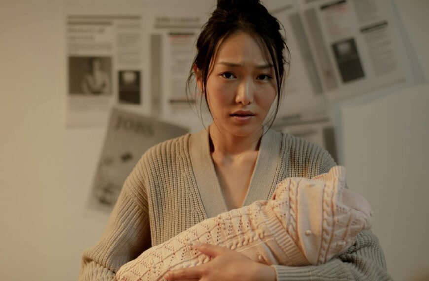 A concerned mother embraces her newborn indoors, surrounded by newspaper articles.