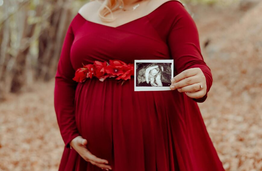 Expecting mother in red dress showing ultrasound in a serene autumn forest setting.