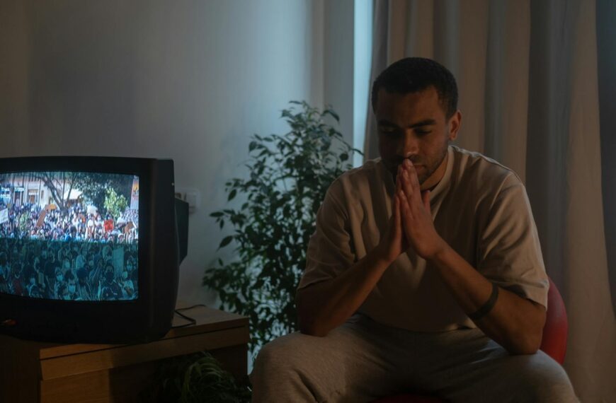 A man seated indoors in reflection during quarantine, TV on.