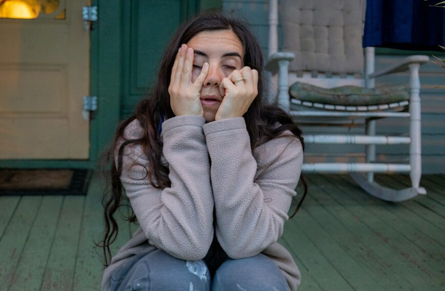 a woman sitting on a porch covering her eyes