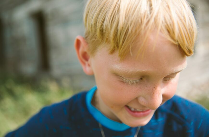 selective focus photography of boy in blue shirt looking down near house