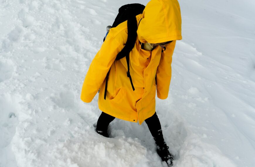 person in yellow coat and black pants standing on snow covered ground during daytime