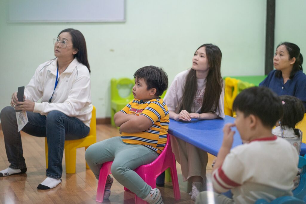 Adults and children sitting in a classroom setting.