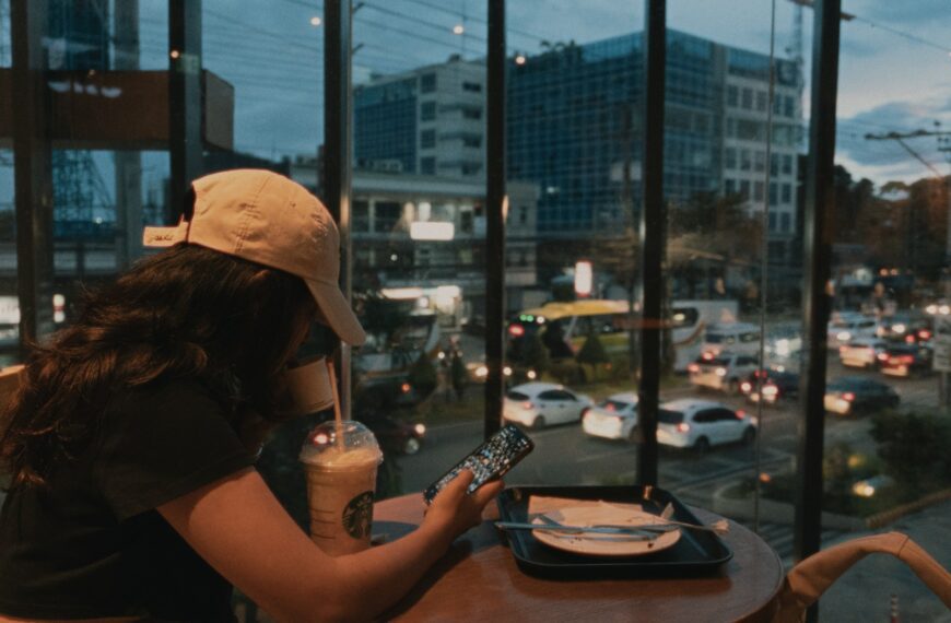 Woman sits with drink, views busy city street.