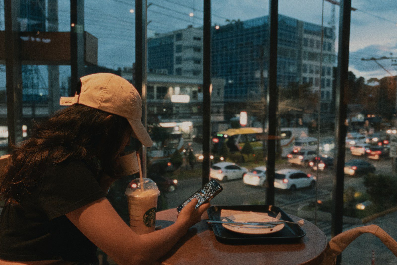 Woman sits with drink, views busy city street.