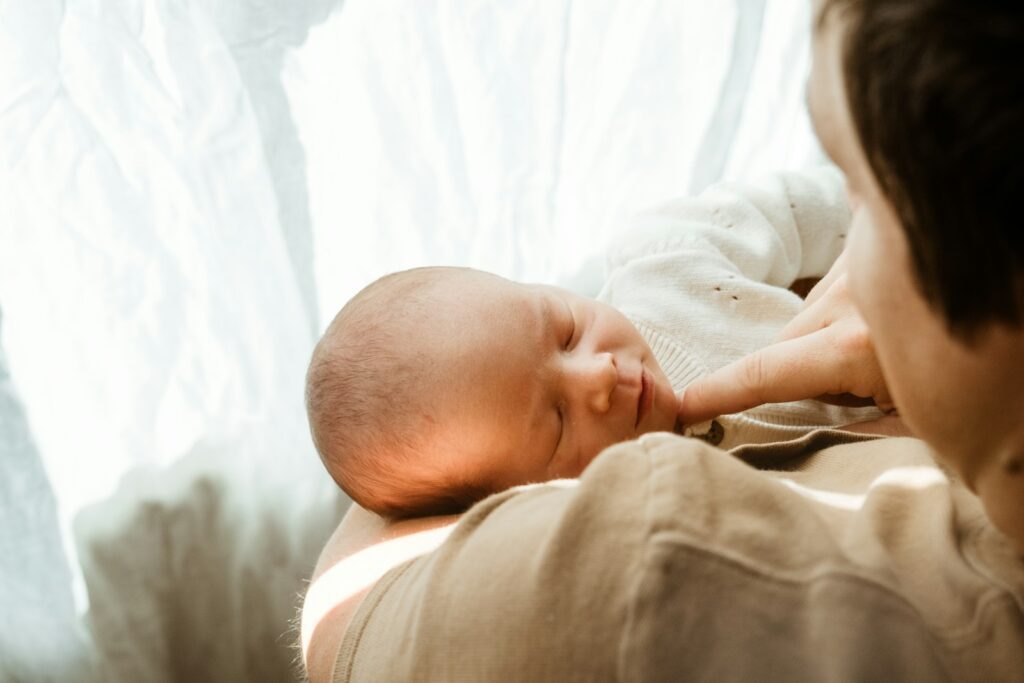Parent holding sleeping newborn baby near window