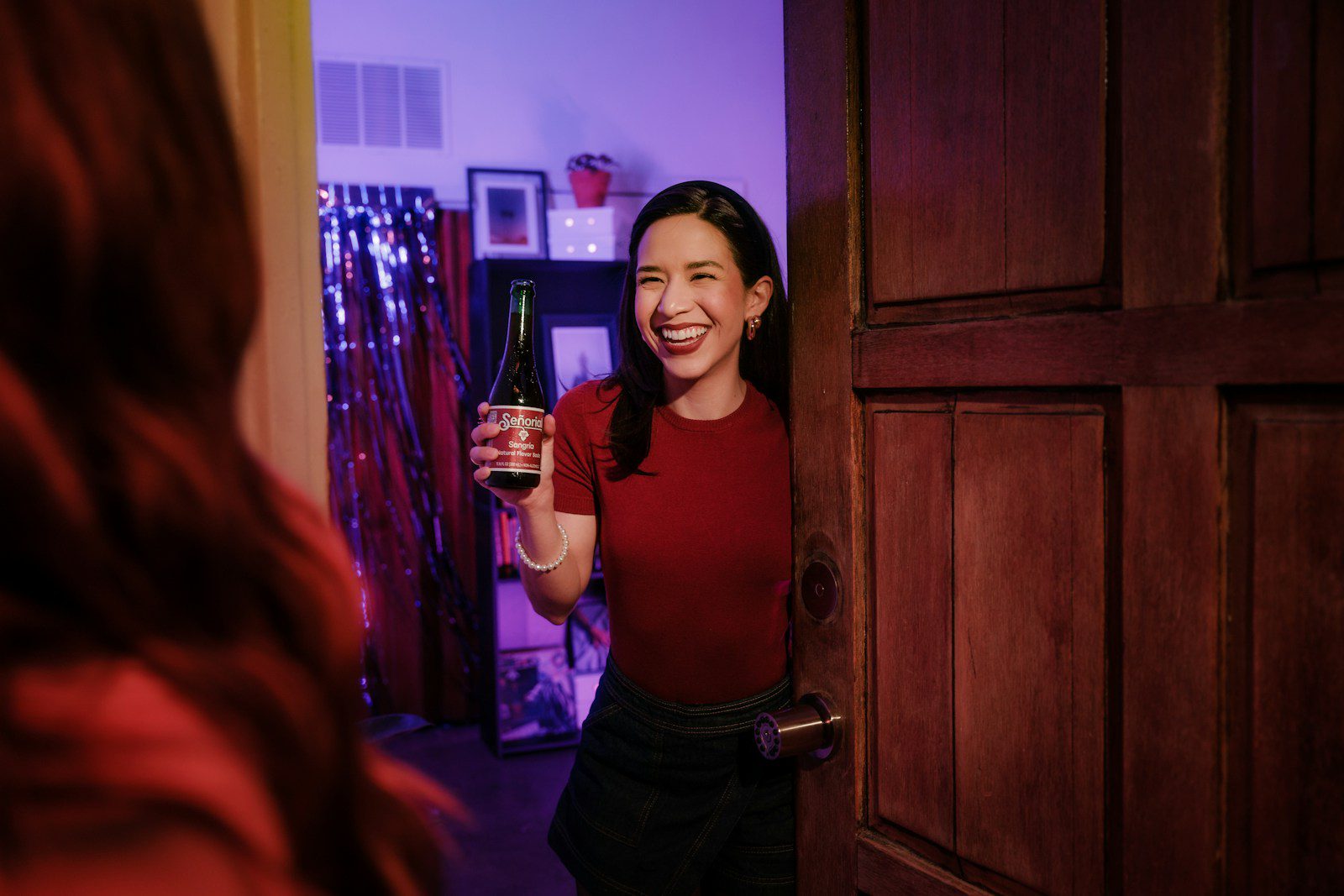 Woman greets guest with a bottle of beer.