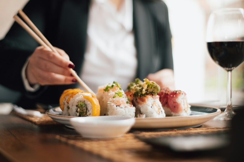 Person eating sushi with chopsticks and wine.