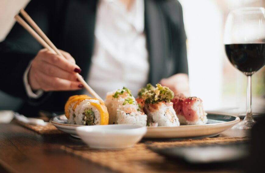 Person eating sushi with chopsticks and wine.