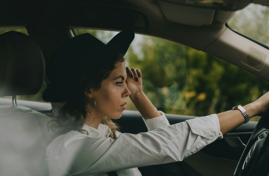 a woman sitting in a car with her hand on the steering wheel