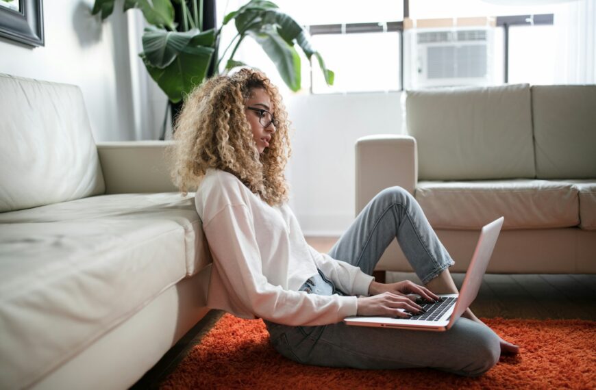 woman sitting on floor and leaning on couch using laptop