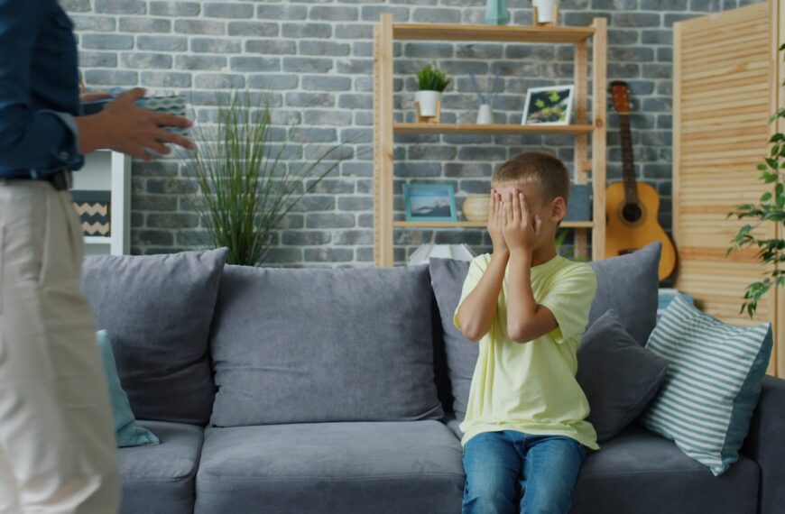 Child hides face while adult stands nearby.