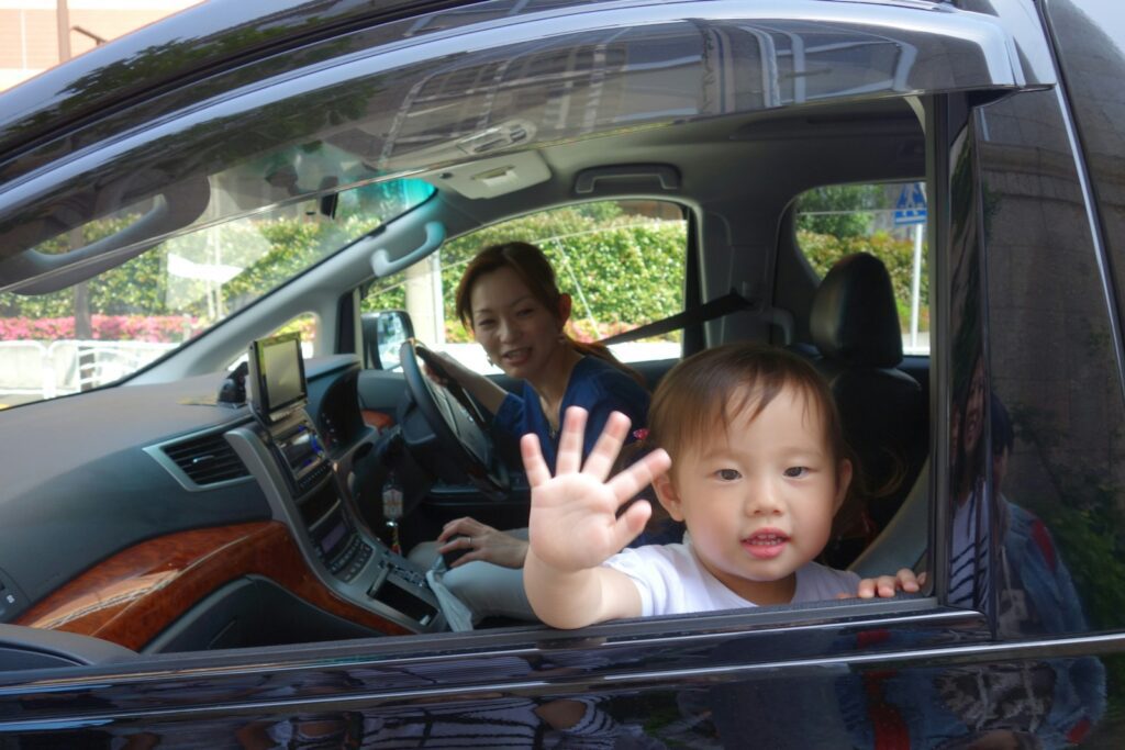 Child waves from car window with mother driving