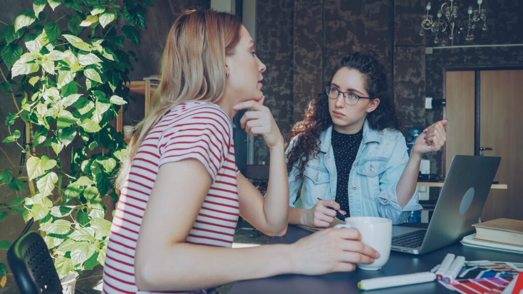 Two women are discussing something over a laptop.