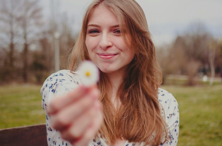 a woman pointing at the camera with a flower in her hand