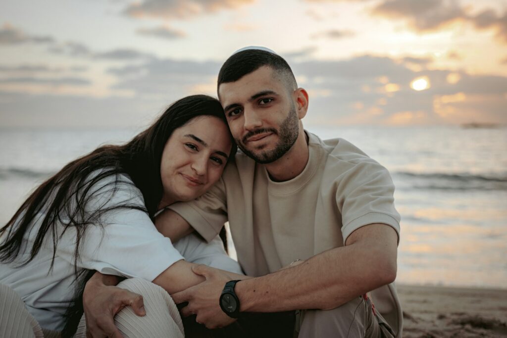 a man and woman sitting on a beach next to the ocean