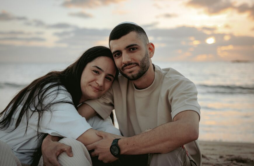a man and woman sitting on a beach next to the ocean