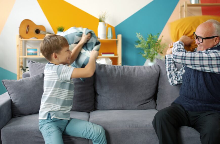 Boy and grandfather having a pillow fight on sofa.