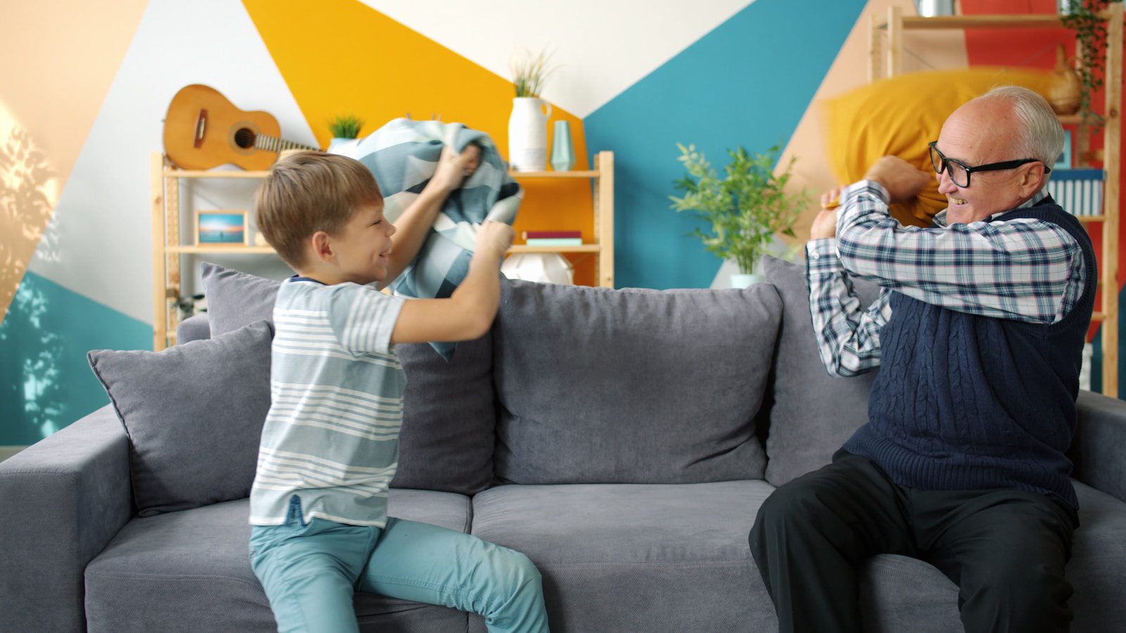 Boy and grandfather having a pillow fight on sofa.