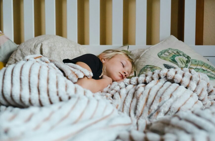 a little girl sleeping in a bed with a blanket