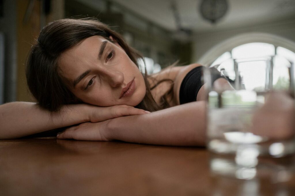 Pensive woman resting her head on a wooden table with a glass of water nearby, indoors.