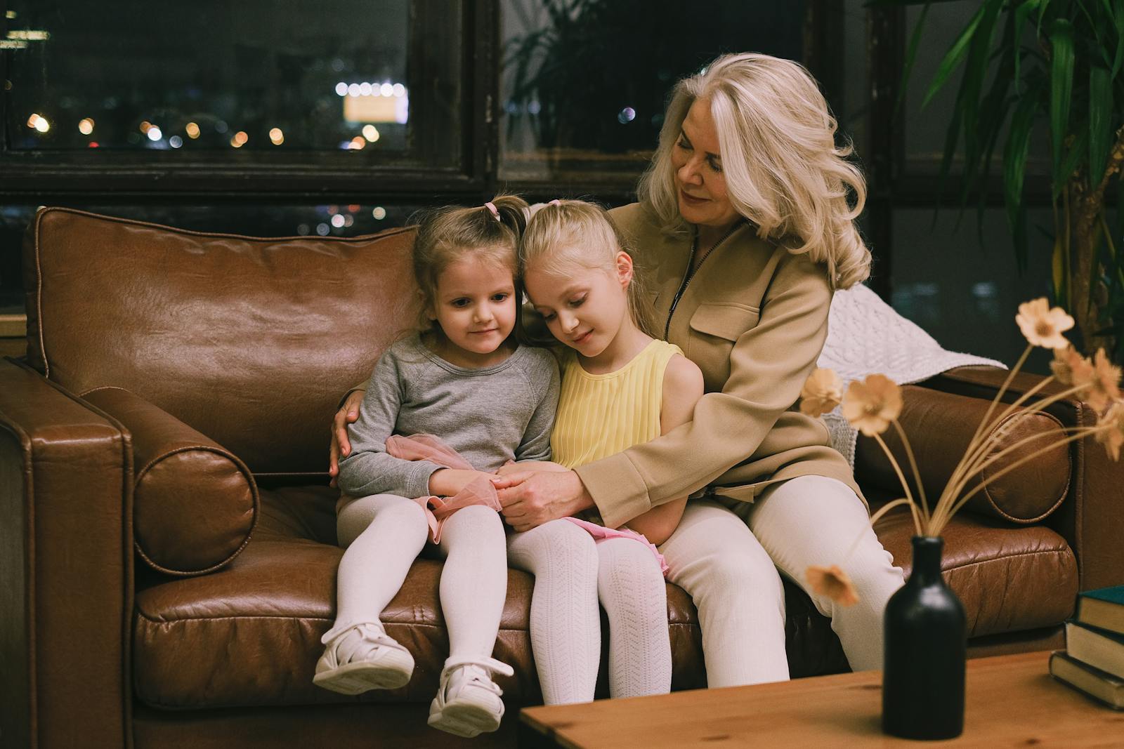 Grandmother lovingly embraces two granddaughters on a cozy leather sofa indoors.