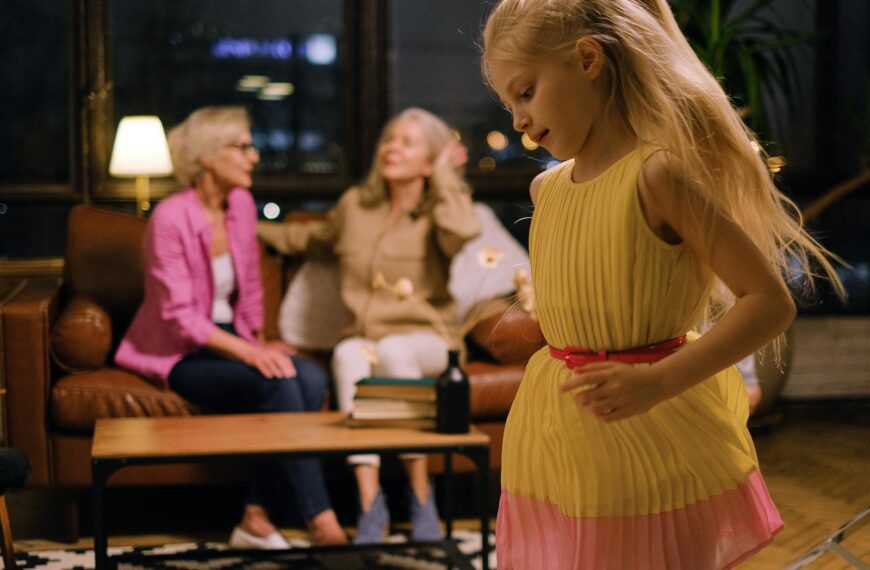 A joyful young girl in a yellow dress dances inside while family members relax on the couch.
