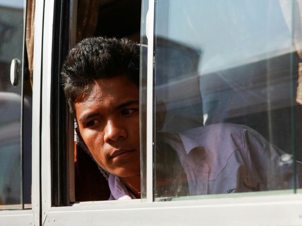 A young man gazes thoughtfully out a bus window, capturing a moment of reflection.