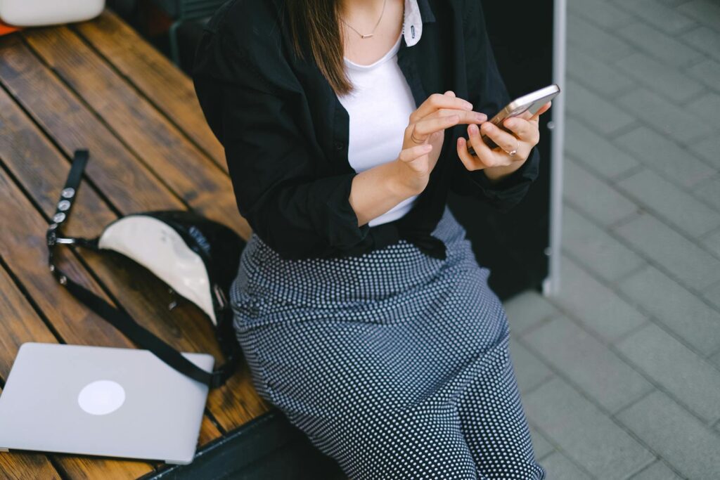 A stylish woman sits outdoors using her smartphone, embodying modern freelance lifestyle.