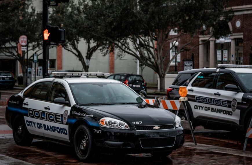 City of Sanford police cars parked on wet urban streets with traffic signals and buildings.