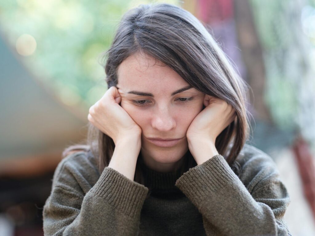 Portrait of a young woman looking pensive and thoughtful while sitting outdoors.
