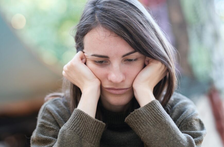 Portrait of a young woman looking pensive and thoughtful while sitting outdoors.