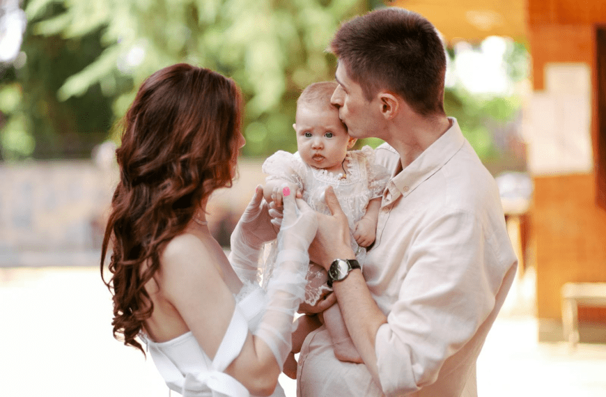 Happy young parents lovingly embracing their baby in a sunny outdoor setting.