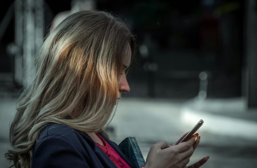Side profile of a young woman texting on her smartphone in a shaded outdoor area.