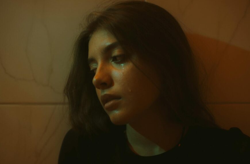 A young woman with brunette hair, expressing sadness indoors, with a dramatic lighting effect.