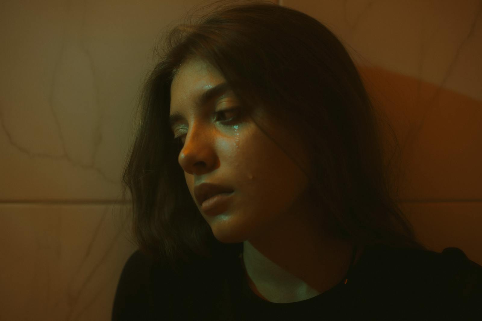 A young woman with brunette hair, expressing sadness indoors, with a dramatic lighting effect.