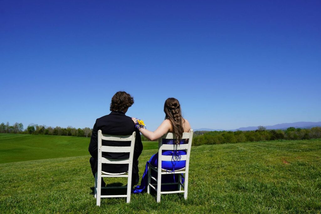 Couple sitting together on white chairs in a vast countryside field enjoying a bright blue sky.