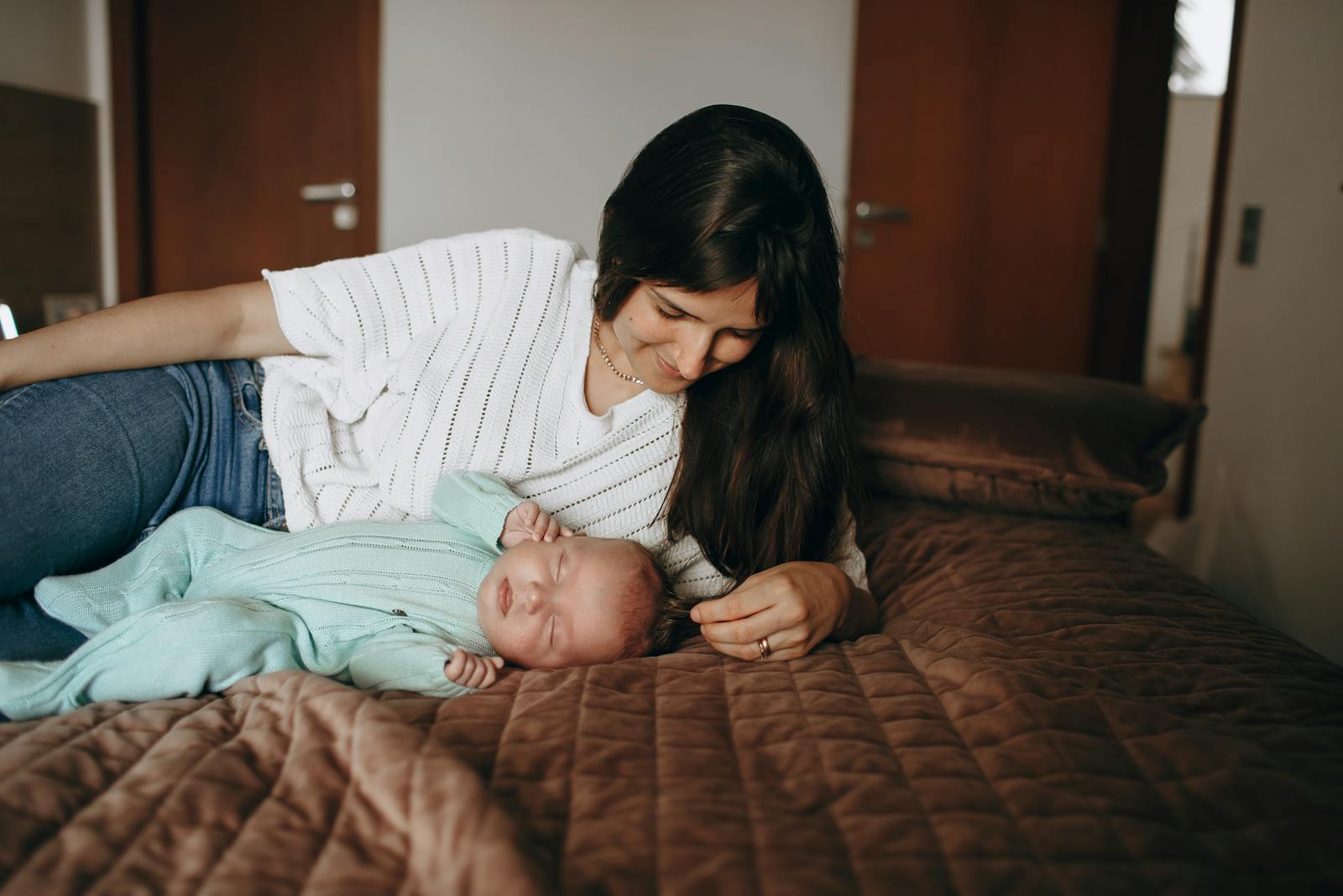 A mother lovingly watches over her sleeping newborn in a warm and intimate bedroom setting.