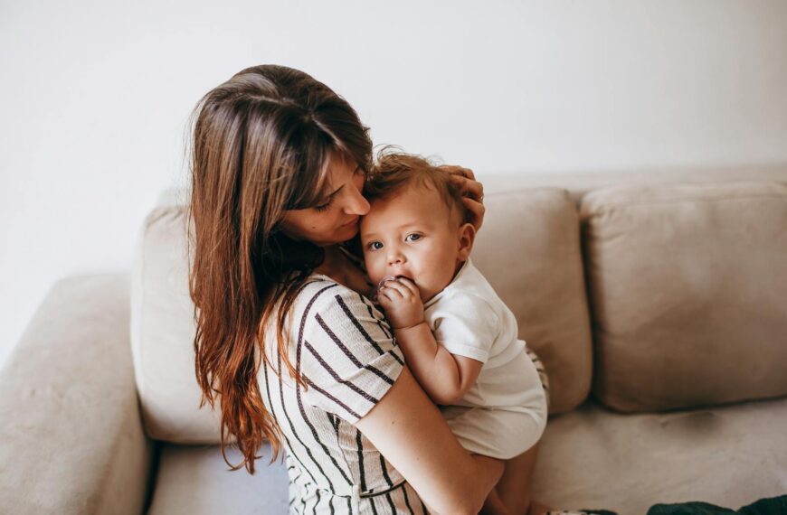 A tender moment between a mother and her baby, expressing love and warmth on a cozy home sofa.