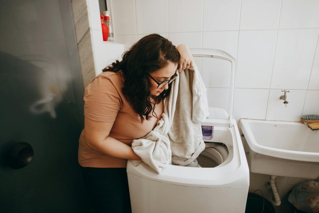 Woman loading a washing machine with laundry indoors. Domestic life in modern laundry room.