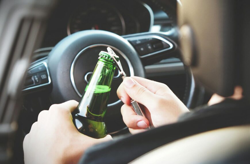 Hands opening a beer bottle inside a car, highlighting the importance of safe driving and awareness of road dangers.