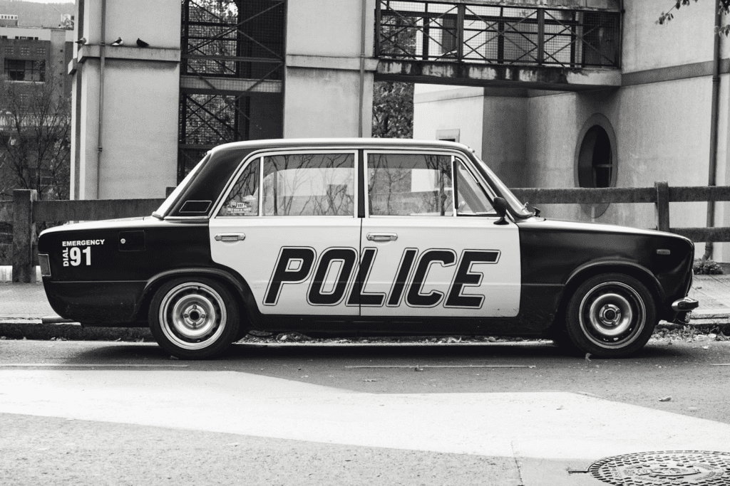 Black and white image of a retro police car parked on a city street.