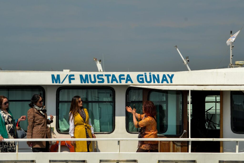 Three women conversing and enjoying a boat tour on M/F Mustafa Günay against a clear sky.