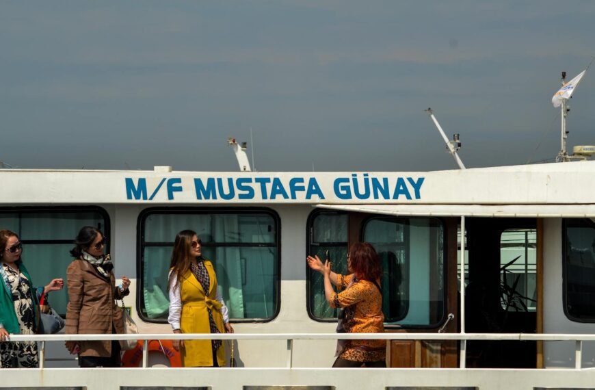 Three women conversing and enjoying a boat tour on M/F Mustafa Günay against a clear sky.