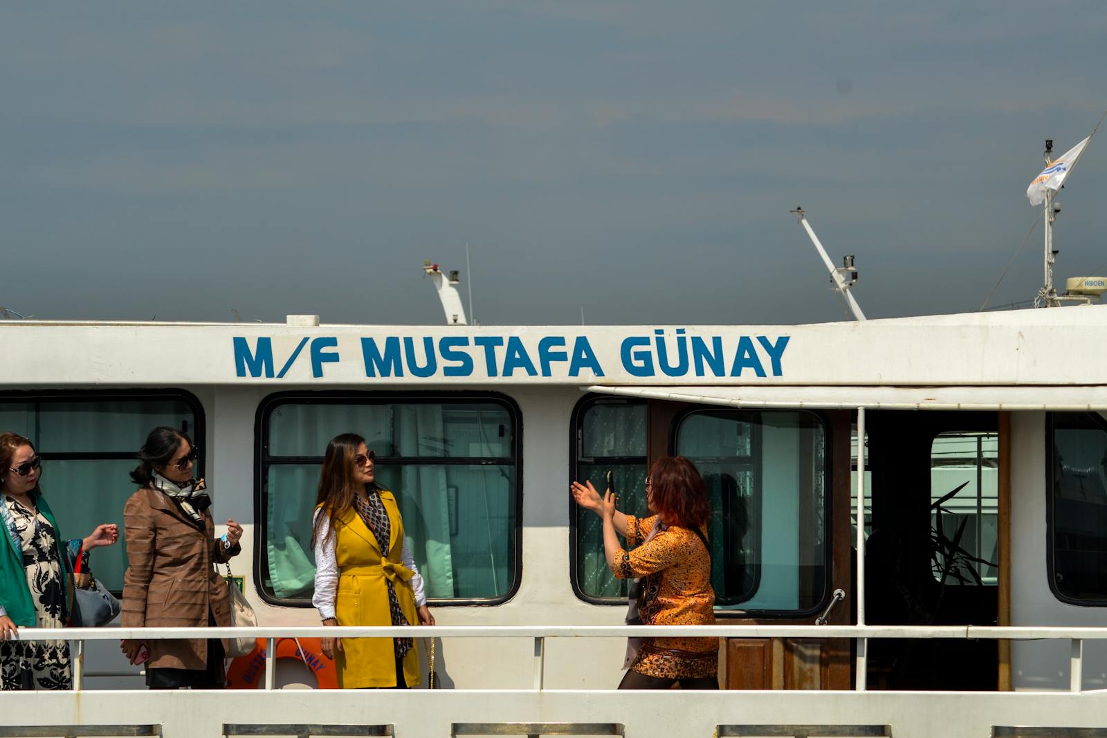 Three women conversing and enjoying a boat tour on M/F Mustafa Günay against a clear sky.