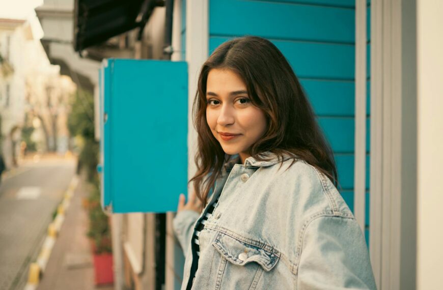 Portrait of a young woman in a denim jacket outdoors by a blue wall.