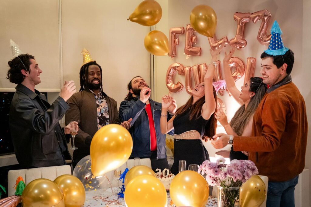 Group of friends celebrating birthday indoors with balloons and party hats.